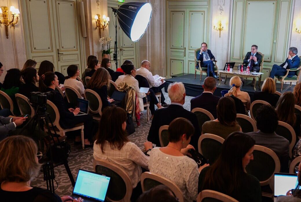 Une salle d'une cinquantaine de personnes face à une table ronde de trois intervenants, dans un salon parisien.